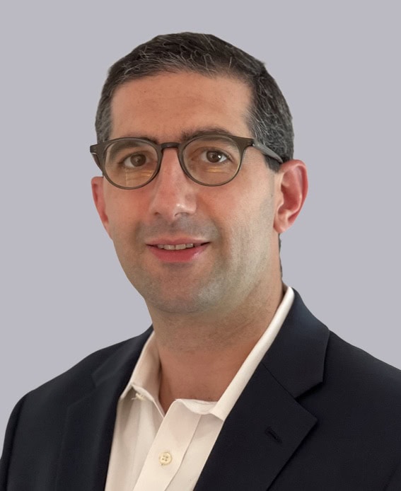 Professional headshot of Dr. Zachary Soloman wearing glasses, a dark blazer, and a white shirt, smiling against a light gray background.