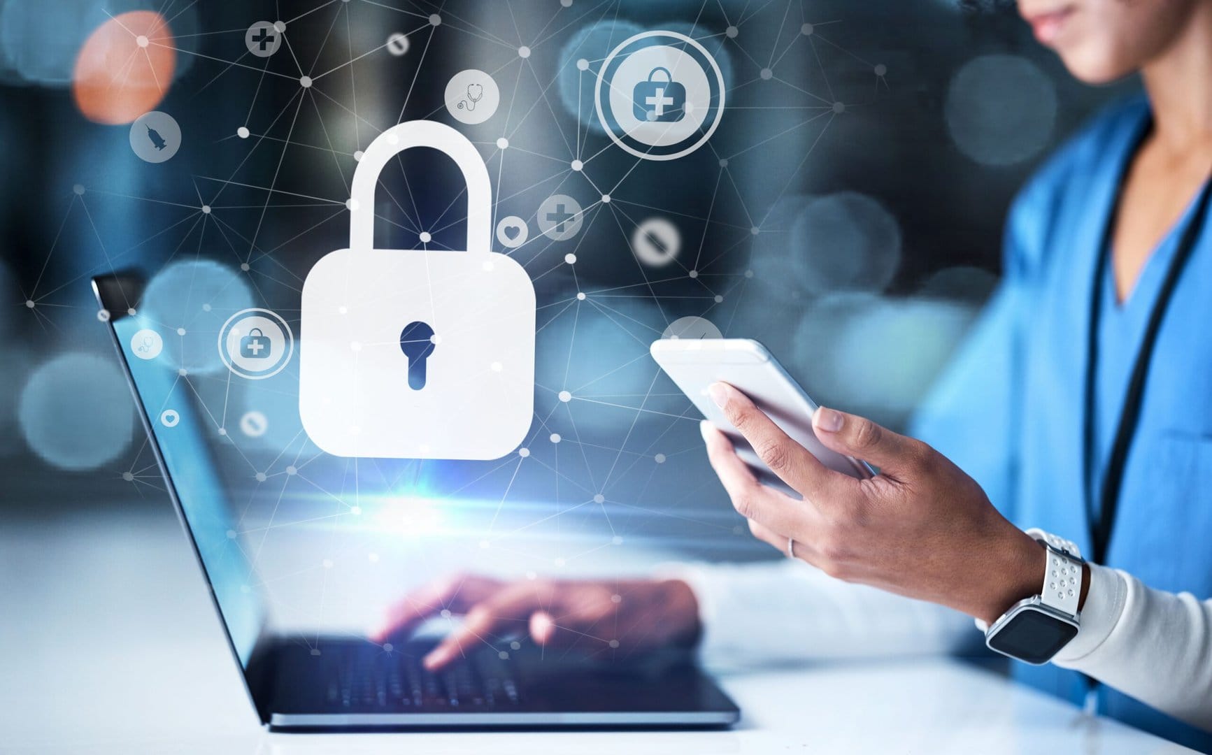 Medical professional on laptop and phone with cybersecurity graphic.