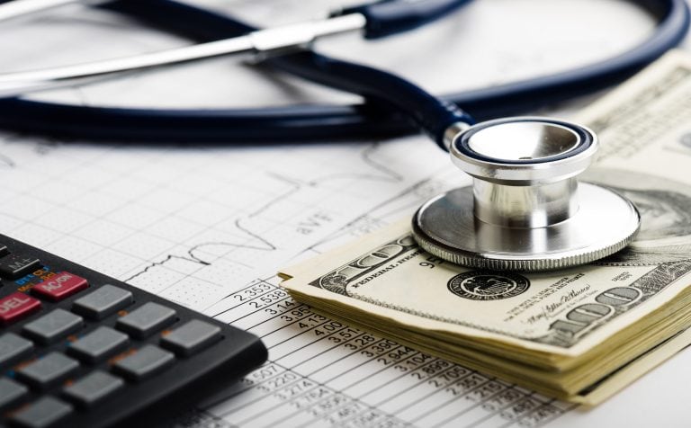 Stethoscope holding down money with calculator and charts